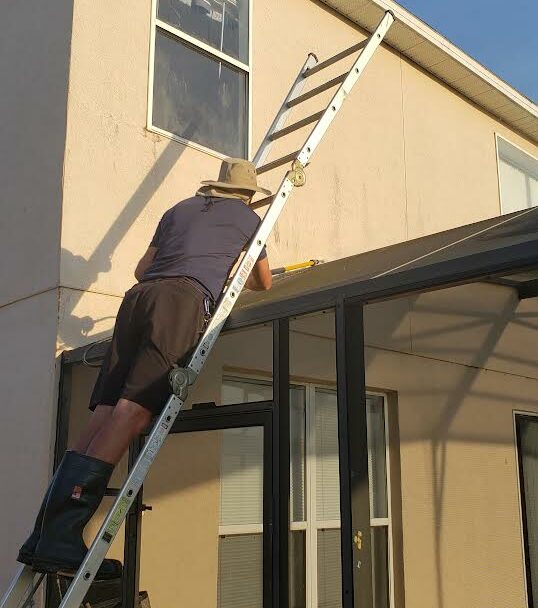 Man standing on ladder power washing a roof in Kissimmee, FL