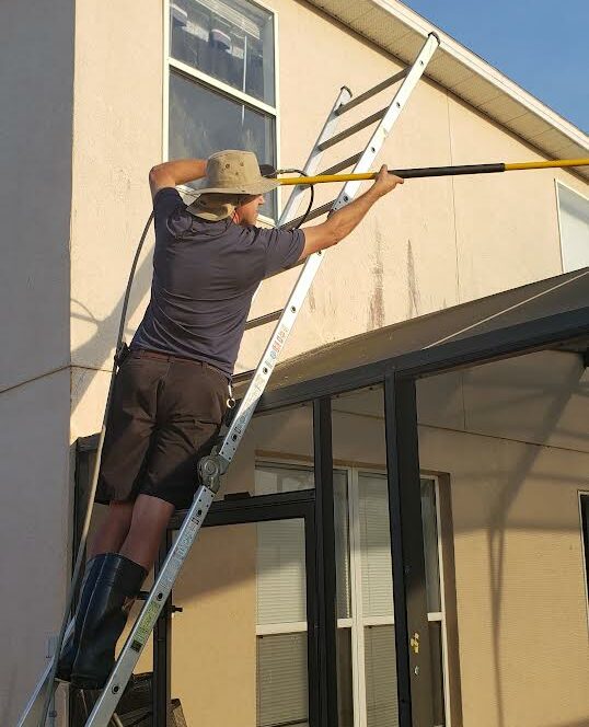 Man on a ladder pressure washing a screen enclosure in Kissimmee