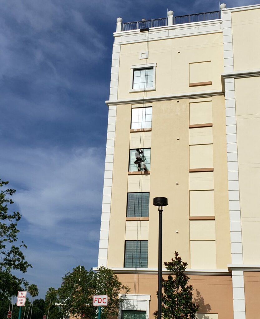 Professional window cleaning hanging halfway down a 5 story building whiled harnessed in.