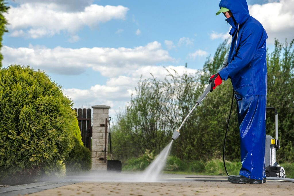 Man pressure washing a driveway in Kissimmee while dressed in a full blue cleaning garment.