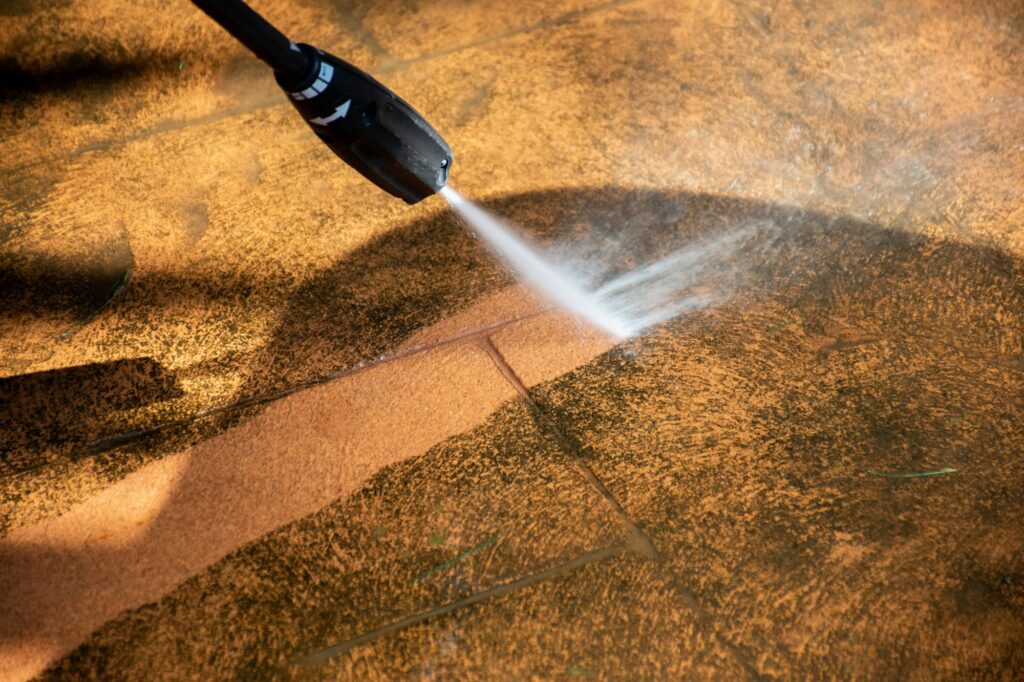 Up close image of the nozzle of a pressure washer cleaning the dirt form a tile floor.